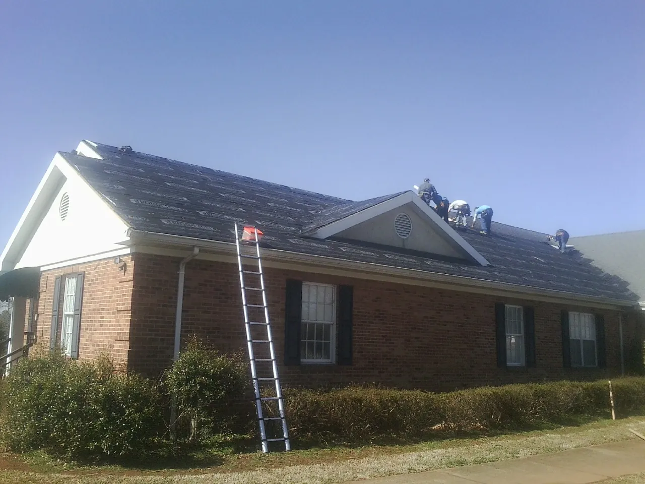 Crew tearing shingles off a brick ranch roof with a ladder set — Metal Roof Repair work by our crew in Flagler