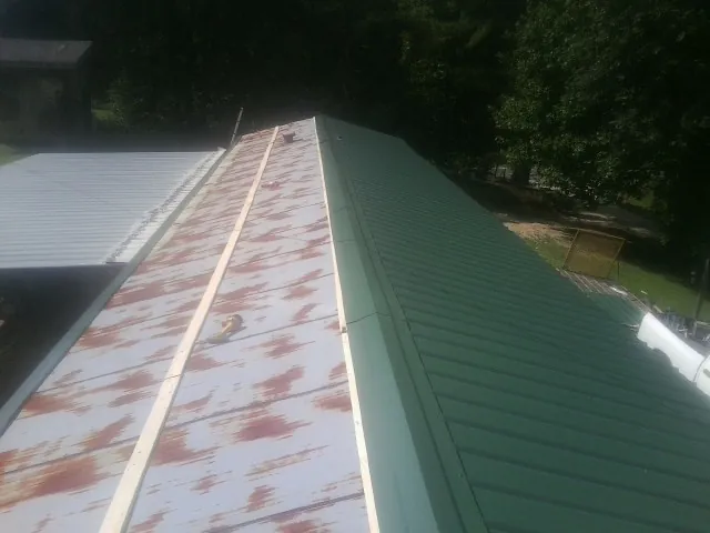 Old rusted panels beside newly installed green metal roofing — Wind Damage Roof Repair by Roofing Brothers in Flagler