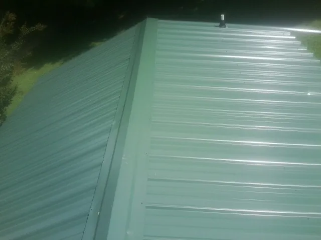 New green metal panels meeting at the ridge of a roof — Flat Roof Repair work by our crew in Flagler