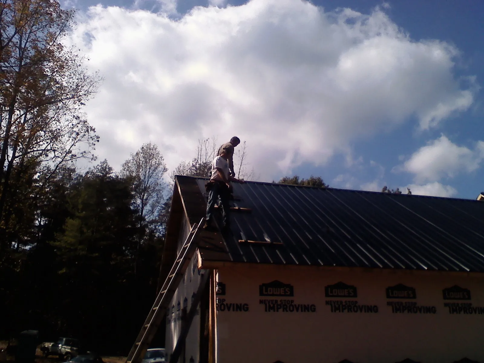 Roofer fastening dark metal panels high against a cloudy sky, from a Roof Inspection job in Flagler